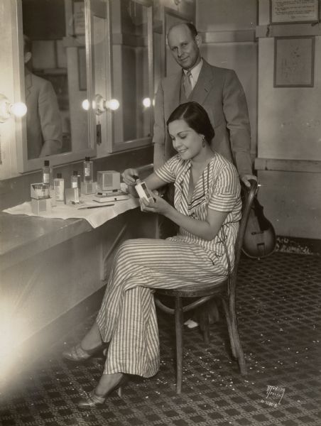 Reri (Anne Chevalier), Tahitian star of the Fanchon and Marco "Tahiti" show at the Orpheum theater trying Cinderella cosmetics in her dressing room with Mr. Sinykin from Cinderella cosmetics.