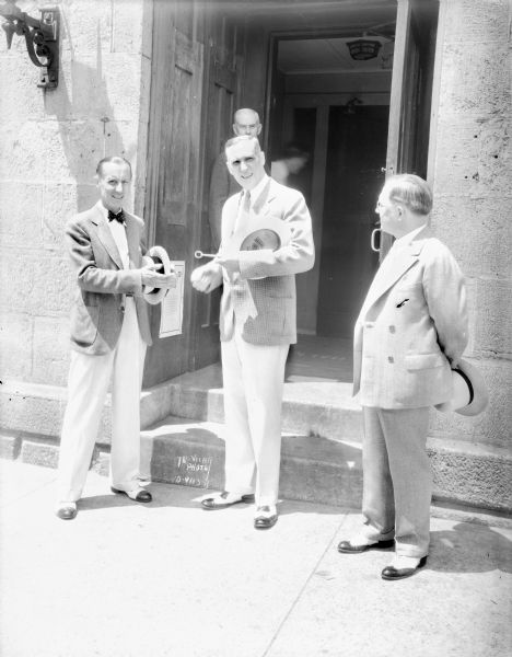 Mayor James R. Law presenting the keys of the city to Chic Sale, former Dane County land owner and character impersonator performing at the Orpheum Theater, on the steps of city hall with Hugh Glannery, Orpheum theater manager, looking on.