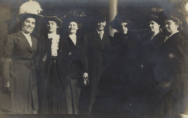 Seven people are posing together. The women are wearing coats and dresses, and the man in the center is wearing a coat and necktie. The postcard was addressed to Mrs. Frank [Josephine] Pierstorff, Middleton, and the caption on back reads: "How do you like the office force of the State Board of Health and Vital Statistics? We are a rather happy looking family, don't you think? Mailed you a letter this morning. Lovingly, May."