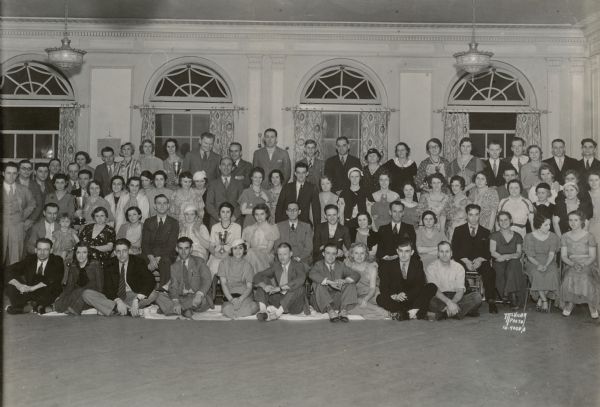 Group portrait of Hill's Dry Goods Store employees at dinner dance party, Schenk's Hall, 2028 Atwood Avenue. A woman sitting in the center, a woman standing on the left, and a woman standing in the back row are holding trophies. Caption in <i>The Capital Times</i>: "About 150 employees of Hill's store and their families took part in a dinner-dance at Schenk's Hall Monday night. The group is pictured above. Dinner was served at 7:30 p.m. and dancing was from 9 to 12. Mrs. Margaret Higbee was awarded a two-day trip to the Century of Progress Exposition for her high sales record."