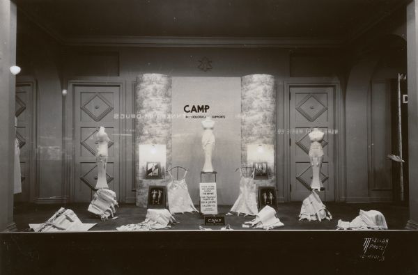 Kessenich display window featuring CAMP physiological / surgical supports made by S.N. Camp & Co. Corset Department. Reflected in the window (reversed) are electric signs for Ward-Brodt Music Co. and Rennebohm Drugs.