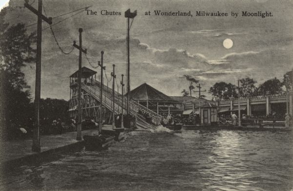Postcard showing a waterslide into a pool by moonlight. People are riding a raft or boat down the slide. Behind the slide is a boardwalk with buildings. Power lines are in the foreground. Caption reads: ", Milwaukee, Wis."Caption reads: "The Chutes at Wonderland, Milwaukee by Moonlight."