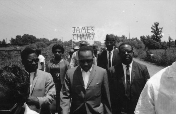 Martin Luther King Jr. marching with a group of people in commemoration of James Chaney, Andrew Goodman, and Michael Schwerner.
