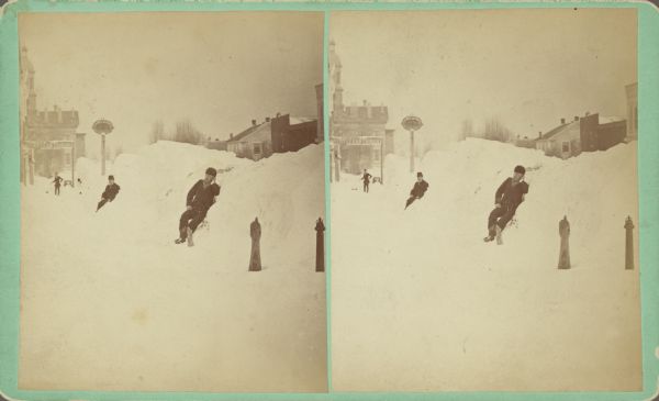 Men posing sitting in snowbanks. A sign over the sidewalk along the left side reads: "Sheboygan Tribune." Written on back of stereograph: "Center St. looking East, taken from Corner 8th St." "Divining height of snow, 12-15 ft."