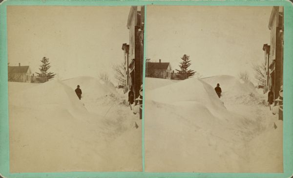 View of men and children posing among snow banks. Commercial buildings are along the sidewalk on the right. Text on the back reads: "Center St. looking west, taken from Corn. 8th Street."