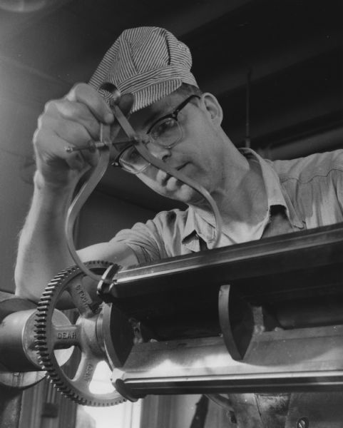 Close-up of a man checking part of a metal lathe with a caliper.