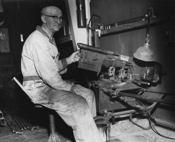 A man is sitting at a machine. He is identified as Julius Balko, 74, of Ladysmith. The Balko family had a company which manufactured boat trailers in Ladysmith, Wisconsin.