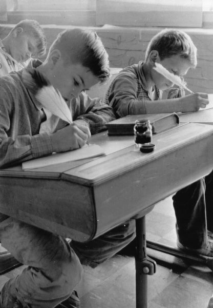 Caption with photograph: "Quill pens with a modern touch are being used by Richard Rice, 12, (left front) and Russell Guth, 10; and behind them is Daniel Nuemann, 12. The Ixonia fifth grade is learning about the schools of 100-yrs ago so the students got into the right mood, with their quill pens. They used turkey and goose feather, in making their pens, but added their own touch by fastening ball points and artists pen points to the quills."