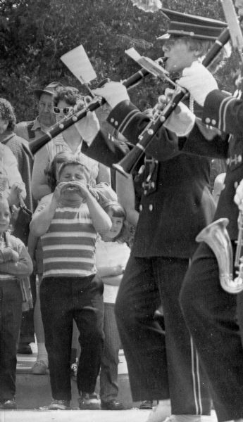 Caption with photograph reads: "Unidentified youngster at left has his own idea on how a clarinet should be played as band passes his curbside bandstand during Alice in Dairyland parade."