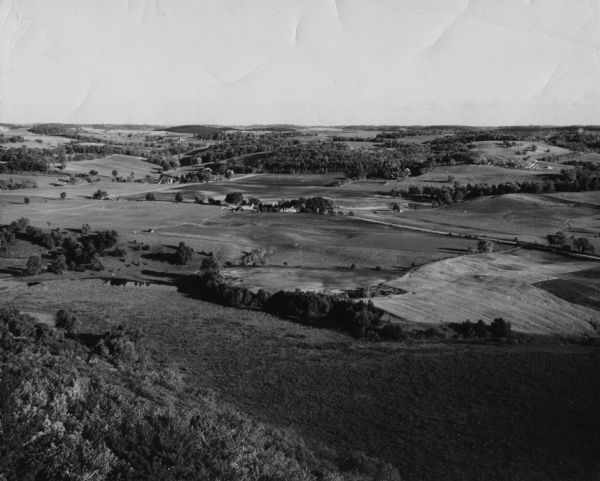 Elevated view of a field, with farmland, roads, houses, and groves of trees.