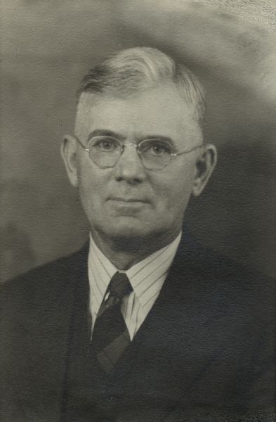 Head and shoulders portrait of a man wearing eyeglasses, and a suit and tie. This is Fred Mero Hunter, a farmer in Burnett county, in the area that would later become Coomer.