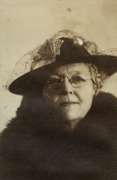 Head and shoulders portrait of a woman wearing a hat, eyeglasses, and a fur coat.