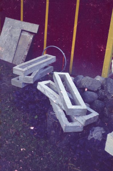 Sculpture pieces are stacked in Sid's backyard near a building, probably the Japanese Tea Pavilion, which is painted red and yellow.