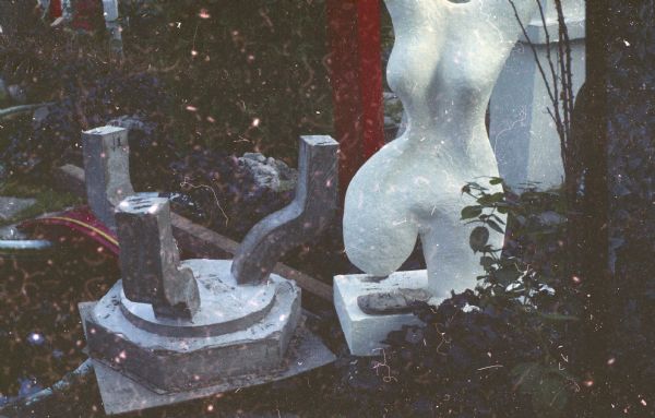 A torso sculpture, and other sculpture parts like a lantern base turned upside down in Sid's backyard.