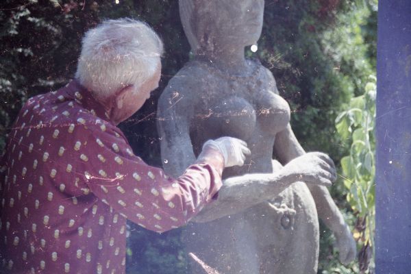 Waist-up view of Sid working on a sculpture inspired by South Asian styles in his backyard. Trees and shrubs are shading the yard.