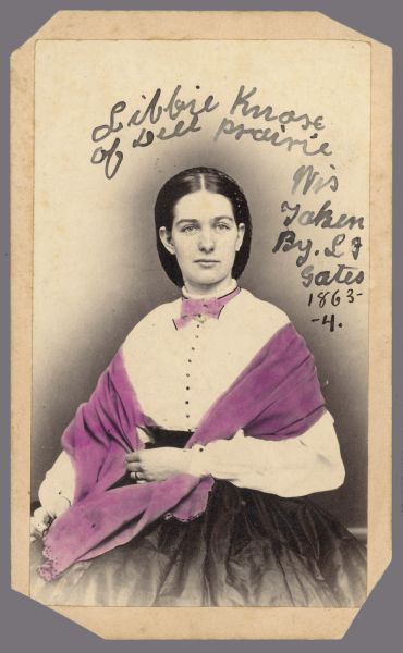 Hand-colored, Carte-de-visite portrait of a woman sitting. Her shawl and her collar have been colored. Written on print: "Libbie Knose of Dell Prairie, Wis. Taken by L.J. Gates 1863-64."