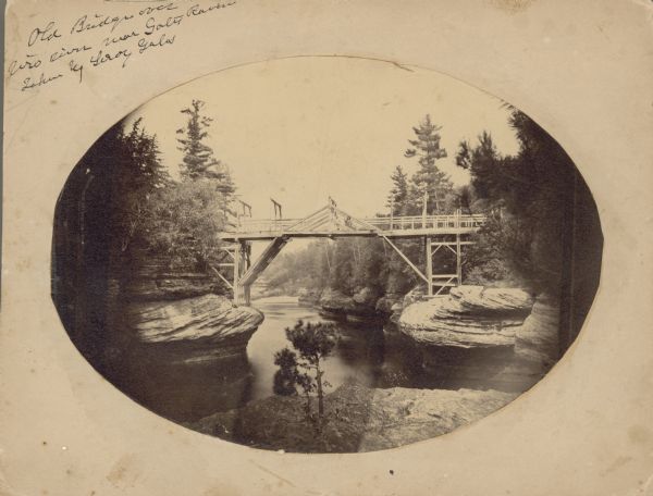 Oval-framed view of old bridge. Written on top left of mat: "Old Bridge over Wis. River near Gates Ravine. Taken by Leroy Gates."