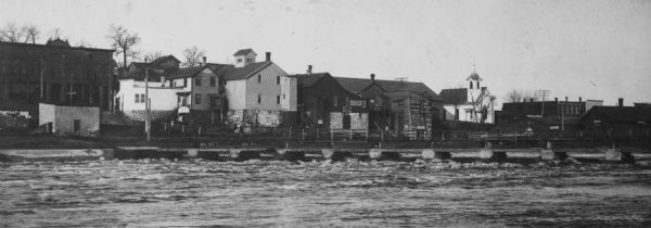 View across a body of water toward several buildings along a shoreline. Caption reads: "Main Street, Necedah, Wis. looking south from the residence of Dr. Canfield. Shows rear side of buildings in [sic] Main Street. Yellow River (?) in foreground. Photo ca. 1904. This print made from a negative loaned to Society by Arthur Murray Kingsbury, St. Paul, Minn."