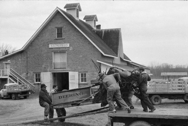 Museum officials and International Harvester truckers unload an 1884 Deering grain binder to store it in Stonefield's main building. Caption reads: "Reaping the harvest, museum officials and IH truckers unload 1884 Deering grain binder (above), store it in Stonefield's massive main building, converted horse barn of Wisconsin's first governor, Nelson Dewey. McCormick's collection encompasses more than a dozen countries and about 4,460 years."