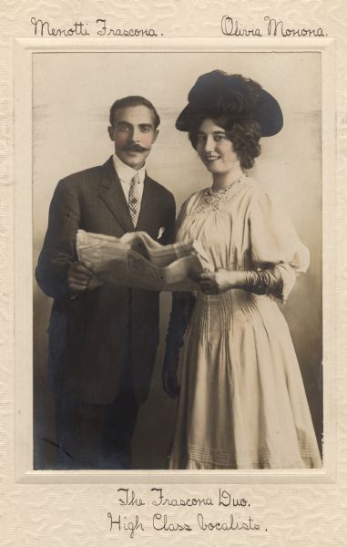 Hand-colored portrait of Olivia Monona and her singing partner, Menotti Frascona. The pair is jointly holding a newspaper. Ms. Monona is wearing gloves.
