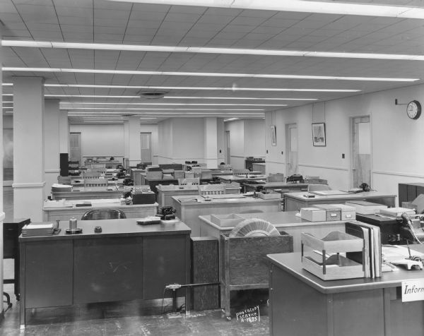Interior view of Ray-O-Vac's large, open fourth floor office with desks and chairs. Behind the desk in the foreground is a large Rolodex in a box on wheels.