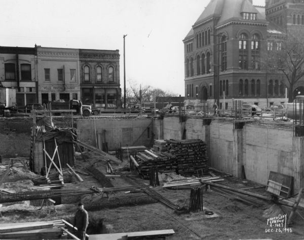 Wisconsin Telephone Co. building site, 122 West Main Street, looking southwest from alley toward West Main Street with construction worker in unfinished basement. Also shows Dane County Courthouse at 207 West Main Street, the Wells Printing Company at 121 West Main Street, and Statz Paints at 123 West Main Street. Building constructed by J.H. Findorff & Son Inc. construction company.