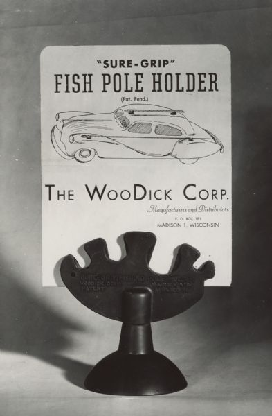 Prototype of "Sure Grip" fishing pole holder for carrying fishing poles on the top or sides of a car. Shows device with an advertising card attached that is featuring the various uses of the device on an automobile. Taken for Halbert M. Wood, WooDick Corporation. Text on holder reads: "Sure-Grip Fishing Pole Holder, Woodick Corp. Madison, WIS. Applied for Patent."