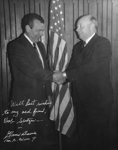 Robert Spitzer shaking hands with Glenn Davis. There is a U.S. Flag behind them. Glenn Davis wrote a message and signed the print which reads: "With best wishes to my old friend, Bob Spritzer, Glenn Davis, M.C. Wis. 9."