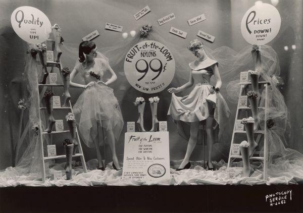 A hosiery window display with mannequins at Hills Store, 202 State Street. A sign in the window reads: "Fruit-of-the-Loom Nationally Famous Nylons, 99 cents to $1.59 New Low Prices." Signs on the wall read: "Compare & Save," "New American Colors for summer," "Heavenly Heels in Luxury 60 ea. Sheers," "Snag Resistant Finish," "Florida Sand," "Kansas Wheat," "Vermont Maple."