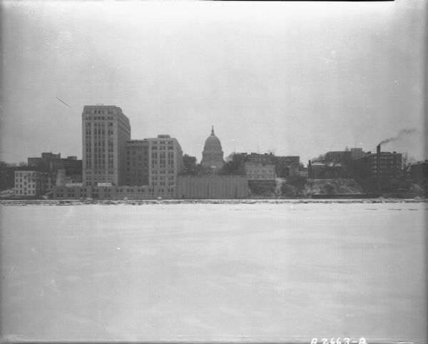 Downtown Madison shoreline taken from Lake Monona in line with Monona Avenue (Martin Luther King, Jr. Boulevard as of January 19, 1987).  Includes Wisconsin State Capitol, State Office Building (2 wings only), 1 West Wilson Street, the Madison Club, 5 East Wilson Street, the Catholic Diocese building, 15 East Wilson Street, and the Bellevue apartment building, 29 East Wilson Street.