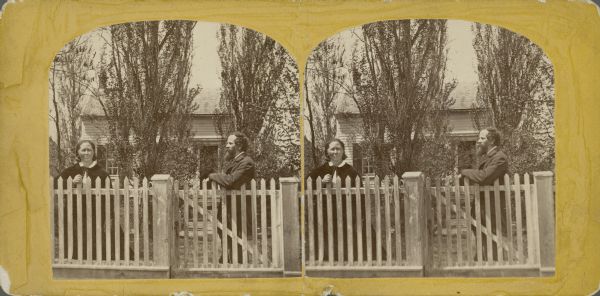 A stereograph of a bearded man, seen in profile, and a woman, looking directly at the camera, posing near a picket fence. There is a small wood frame house in the background nearly obscured by trees. The couple is identified as Eduard and Elise Cunradi Schroeder (alternatively spelled Schroeter). 