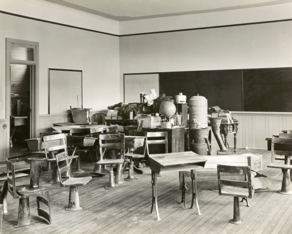 Interior of a school storage room filled with desks and other school supplies, including a Smith Sanitary Bubbler Fountain (may be the origin of the regional term "bubbler" for a water fountain).