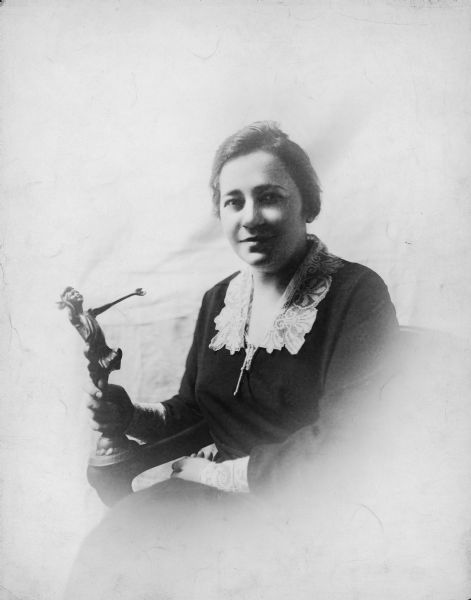 A studio portrait of Renee Harris holding a statuette, which is possibly an award. She is sitting, and is wearing a dark dress with a lace collar.
