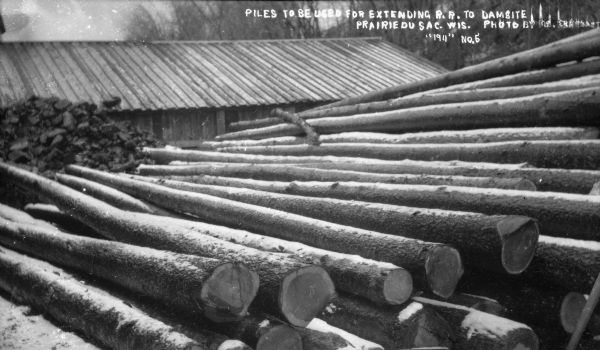 Stack of logs with the caption "Piles to be used for extending R.R. to dam site."