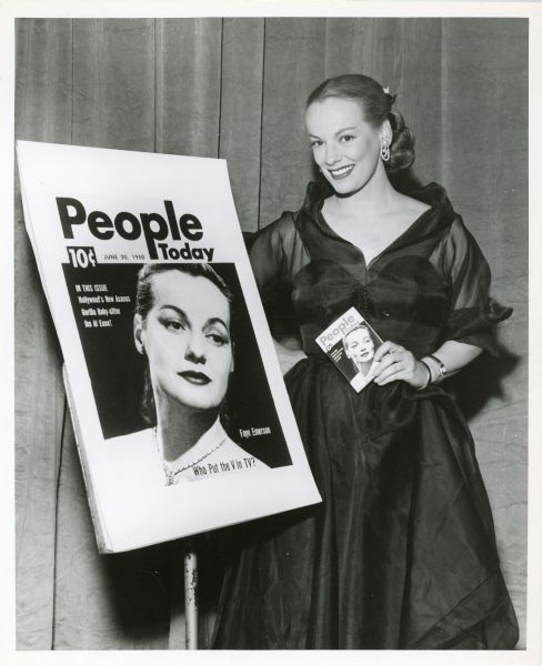 Faye Emerson standing next to an enlarged cover for the June 20, 1950 edition of the magazine <i>People Today</i>. She is featured on the cover. Faye is also holding a copy of the magazine.