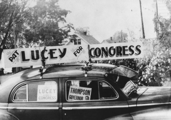 Sign on top of a car promoting Patrick J. Lucey for Congress. Another sign in the window shows support for Carl W. Thompson for Governor.