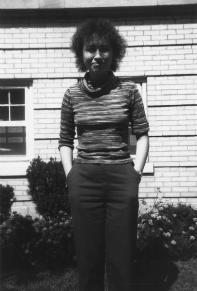 A woman is standing and posing outdoors in front of a building. Caption reads: "Marcella Tardy, organizer, from Kalamazoo, MI."