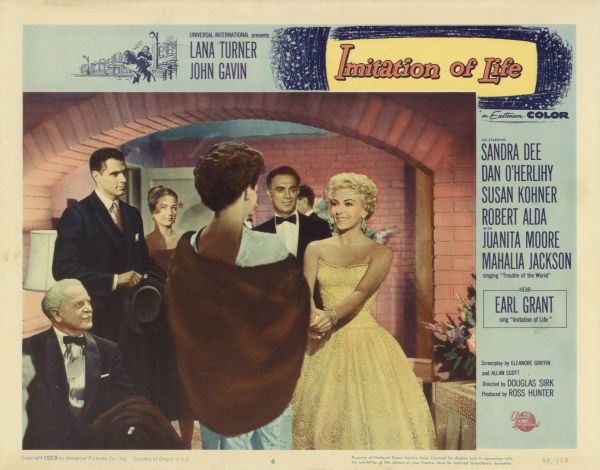Lobby card for the 1959 film "Imitation of Life" starring Lana Turner, Sandra Dee, and Juanita Moore.  The image on the card shows Lora Meredith (Lana Turner) greeting another woman in her dressing room.  There is a group of men and women, all dressed up, in the room as well.