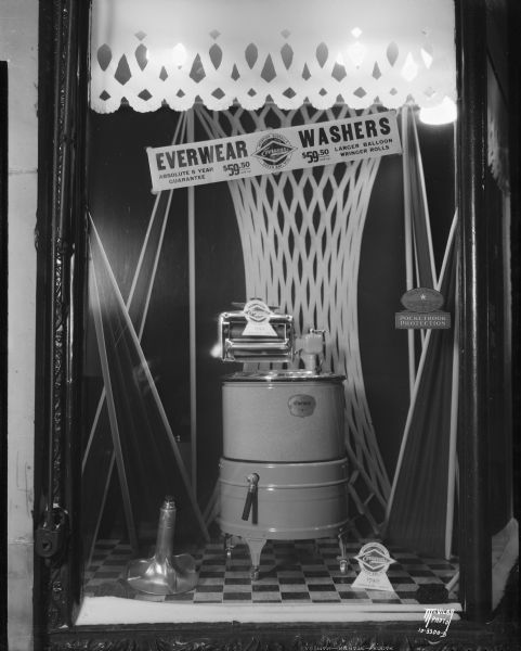 Window display of Everwear clothes washer, alternate view. 116 E. Main Street. A sign above the washer reads: "Everwear Washers, Absolute 5 Year Guarantee, $59.50 and up, Larger Balloon Wringer Rolls." A sign on the floor reads: "McIntyre•Burrall, Est. 1908, Green Bay, Wis. Everwear Washers, Trademark Reg. $79.50 Everwear De Luxe."