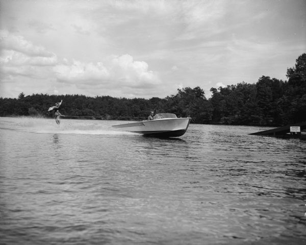 A man is driving a motorboat pulling a man water skiing who is carrying a woman on his shoulders as a part of the Tommy Bartlett Water Ski Show.