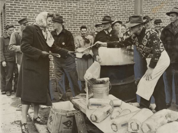 Caption on back reads: "All foodstuffs is confiscated by Red authorities and rationed to the citizens. Mrs. Delbert Bauer is shown as she gets her cup of Pa[sic]tatoe Soup at an out-door kitchen. INP Photo by F. Standfield." Another caption on the back is a newspaper clipping that reads: "When the 'Communists' took control  of Mosinee Monday they set up their own food kitchen. 'Highlight' of the menu was a cup of potato soup which Mrs. Delbert Bauer is receiving here. Sentinel photo."
