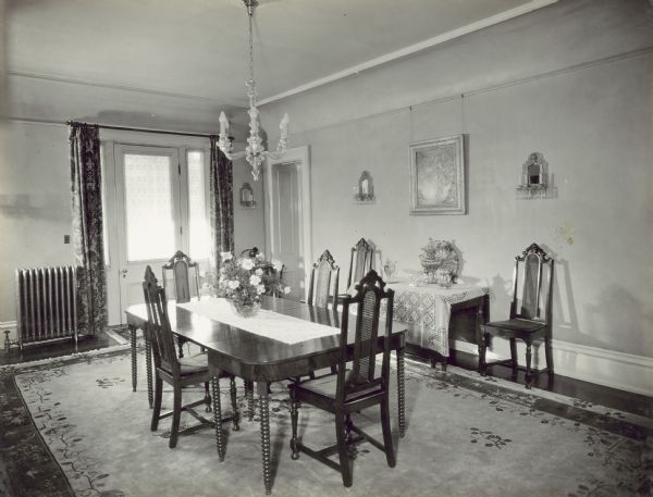 Dining room in the Governor's Mansion. There is a door with sidelights on the exterior wall which leads to the porch, and an interior door in the back right corner which leads to the kitchen. 