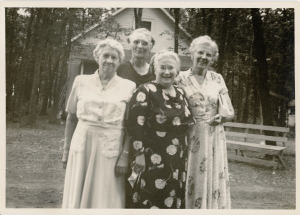 Reverend Melvina Krauss (in front wearing a dark dress) posing with three other women. They are probably members of the Western Wisconsin Camp Association. There is a building in the background.