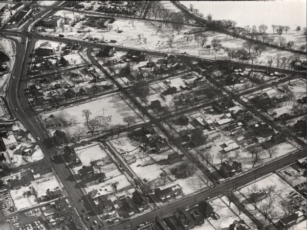 Air view in winter of the Triangle Redevelopment Project looking east with Regent Street running along the left edge, W. Washington Avenue along the top, and S. Park Street angled across the bottom. The former Greenbush neighborhood is significantly thinned, but still visible are St. Joseph Church, School, and convent; a Standard filling station; Gervasi's Store; Paley's Junk Yard; Neighborhood House; Gerke's Junk Yard; and Di Salvo's Grocery and Supper Club.