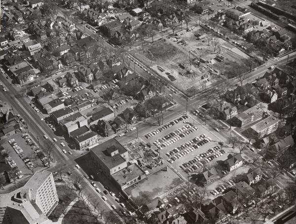 Aerial view with beginning of construction on Sellery Hall on the block bounded by Park, West Johnson, Murray, and West Dayton Streets. Park Street runs from lower left to upper right. University Avenue is at lower left with Chadbourne Hall in the corner. A large surface parking lot filled with cars is on the corner of Park Street and University Avenue opposite the construction.