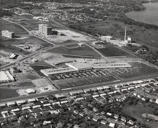 Aerial view of the Hilldale Shopping Center and environs. Anchor store is Gimbels. N. Midvale Boulevard runs left to right. The State Department of Transportation building is under construction to the west in the Hill Farms area. The golf course at the Black Hawk Country Club and a portion of Lake Mendota can be seen at top right.