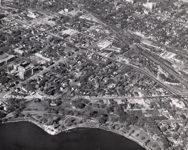 Air view focused on the Greenbush neighborhood of Madison prior to its demolition for the Triangle Redevelopment Project. Monona Bay and Brittingham Park are at bottom. The triangle is bordered by West Washington Avenue, and S. Park and Regent Streets. Railroad roundhouse is at right.