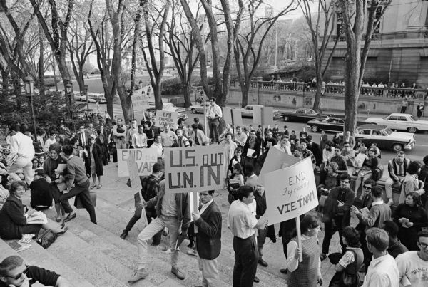 Large group of students gathered on the steps of the University of Wisconsin Memorial Union. Many carry signs urging the U.S. military to leave Vietnam. Langdon Street and the State Historical Society headquarters building are in the background.
