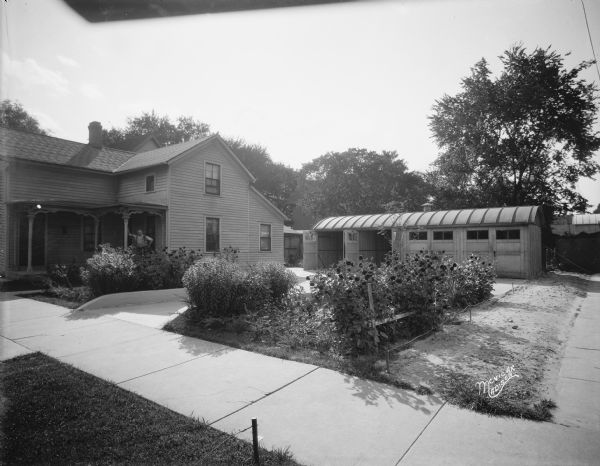 House and flower garden, 614 E. Main Street. There is a man (possibly Emanuel F. Yager) standing on the porch with a Trachte 4 bay garage in the background.
