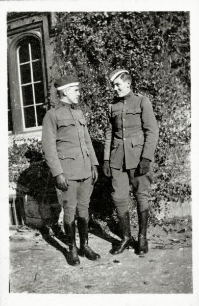 Two men in military uniform posing outdoors together in front of a building. 
